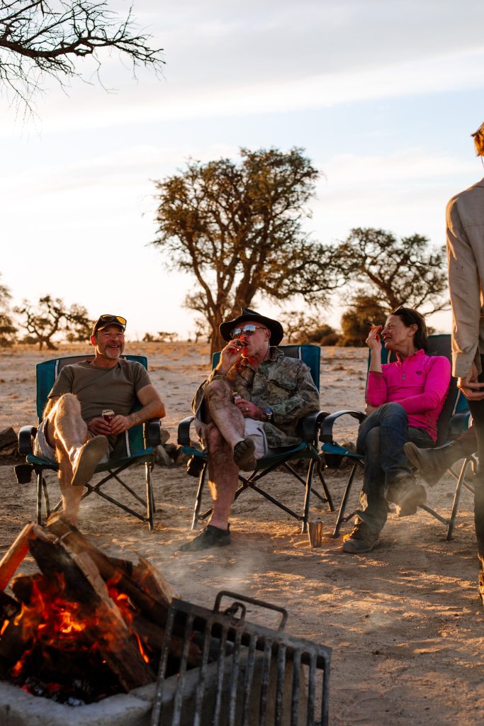 Travellers on horseback safari entertaining each other by the fire in Nambia 