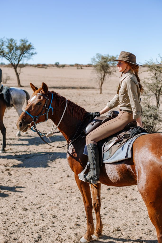 Woman on horse back safari wearing Jodhpurs, sun hat, gloves and glasses 