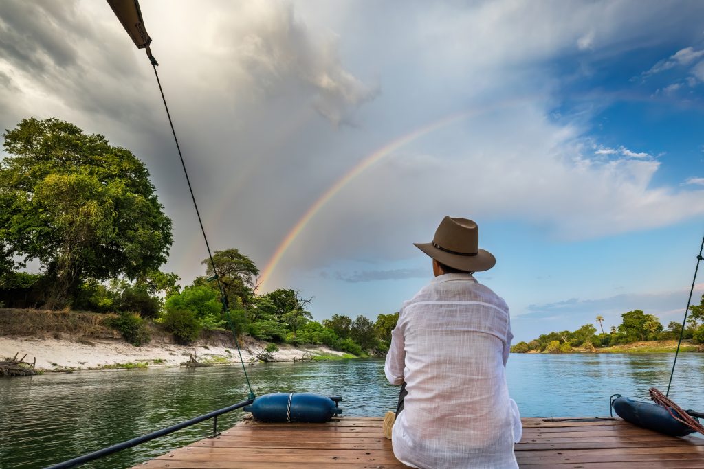 Man looking at two rainbows in the sky whilst sat looking at the scenery at  Chundukwa River Lodge, Zambia
