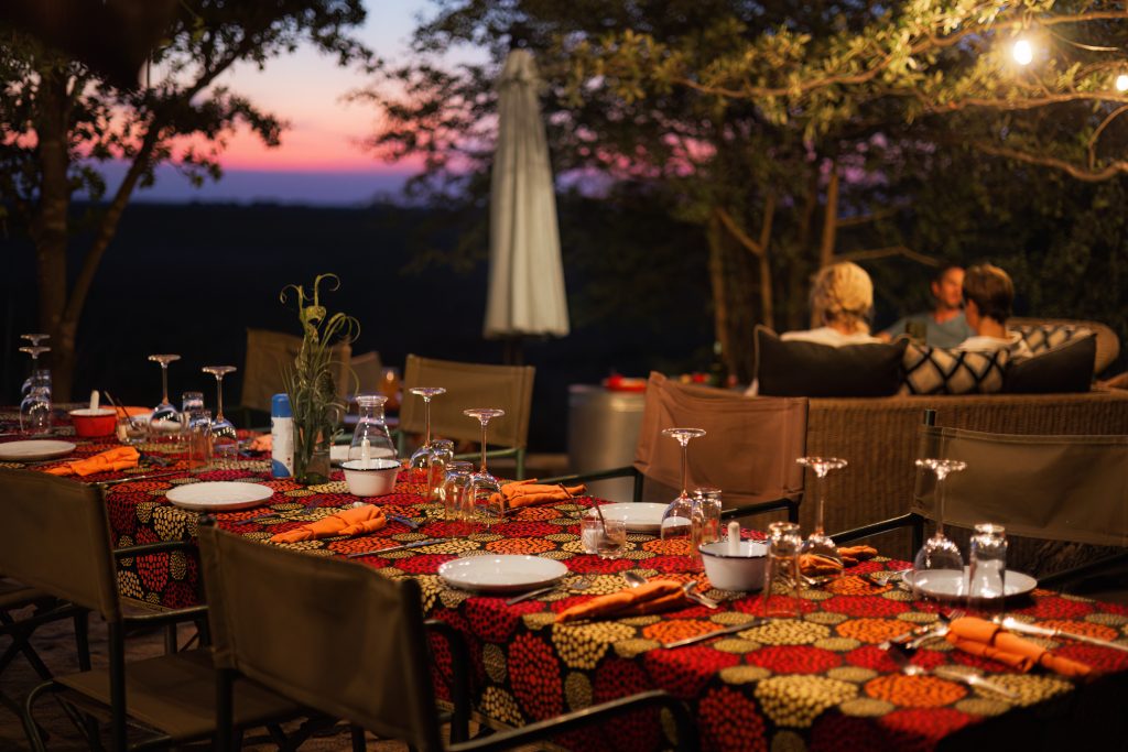 Zambian Horseback Safari Camp tables are ready for dinner and people are sunset viewing in the back ground